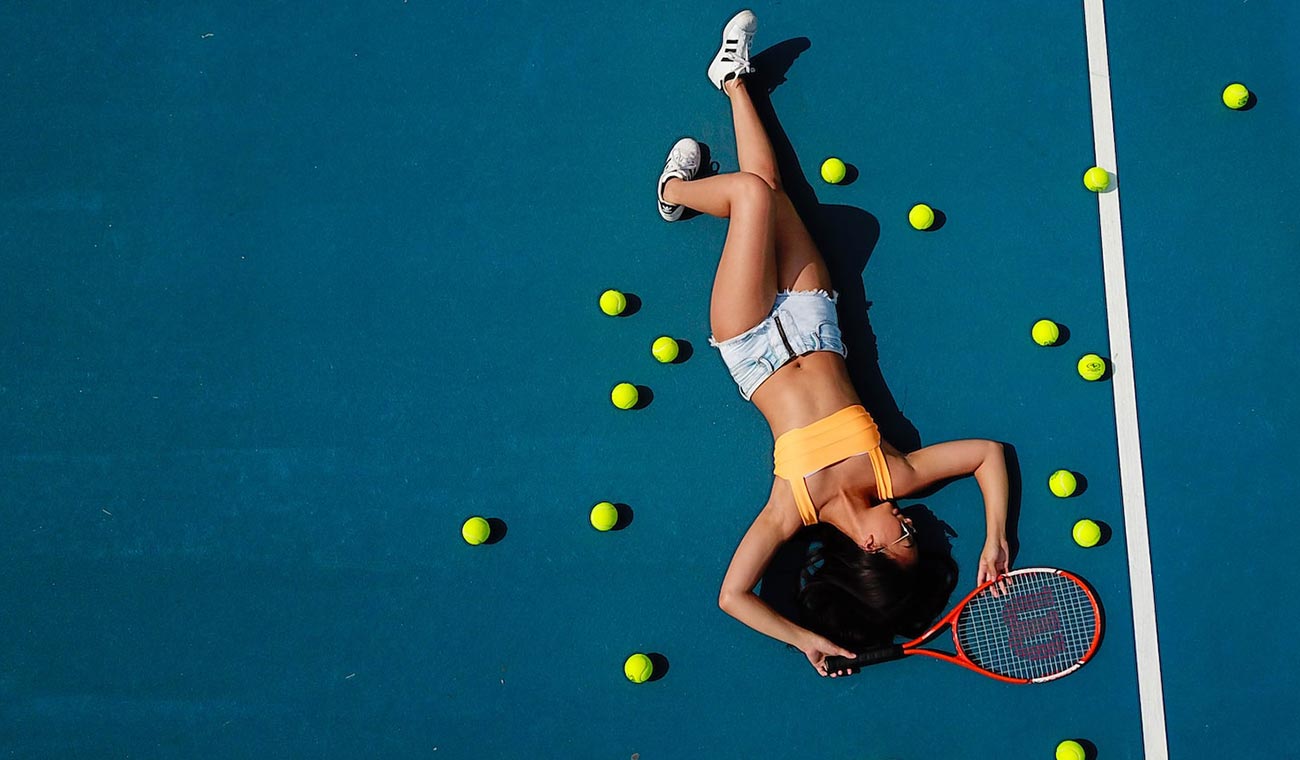 A person is sleeping on a tennis court surrounded by tennis balls.